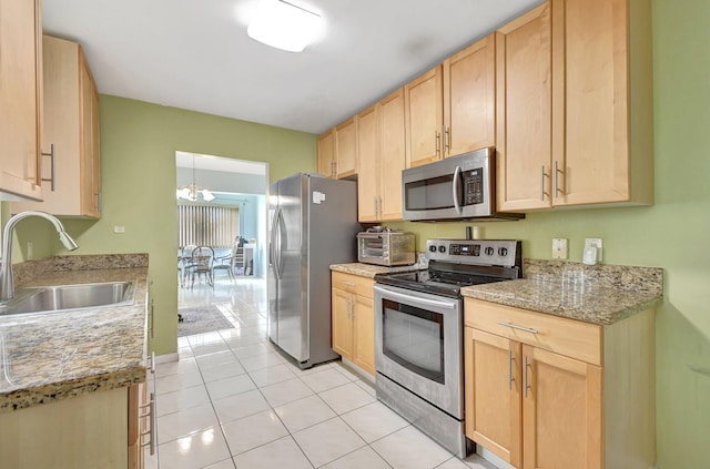 kitchen with sink, appliances with stainless steel finishes, light brown cabinets, light tile patterned floors, and an inviting chandelier