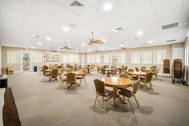 carpeted dining space with a paneled ceiling, ceiling fan, and a healthy amount of sunlight