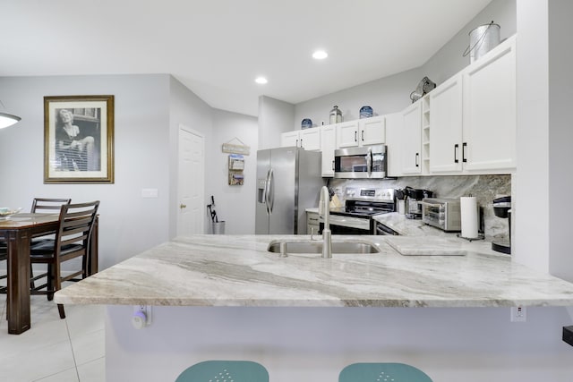 kitchen featuring backsplash, a kitchen breakfast bar, kitchen peninsula, appliances with stainless steel finishes, and white cabinetry