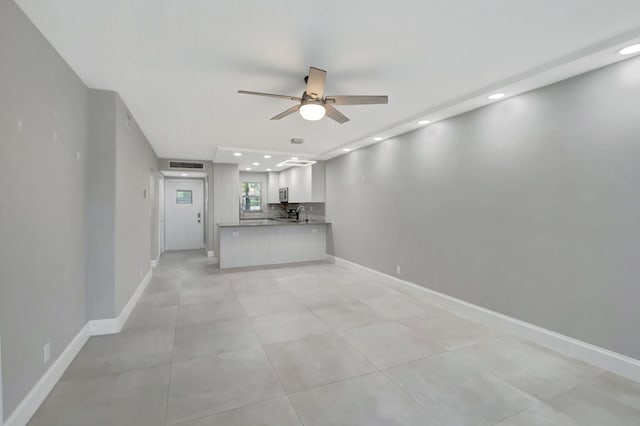 unfurnished living room featuring ceiling fan, sink, and light tile patterned floors