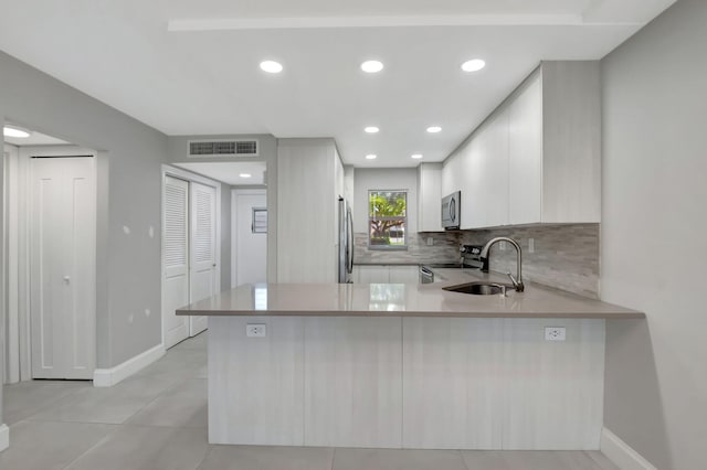 kitchen featuring stainless steel appliances, white cabinetry, backsplash, sink, and kitchen peninsula