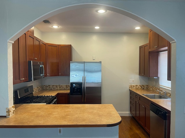 kitchen featuring appliances with stainless steel finishes, kitchen peninsula, sink, and dark hardwood / wood-style flooring