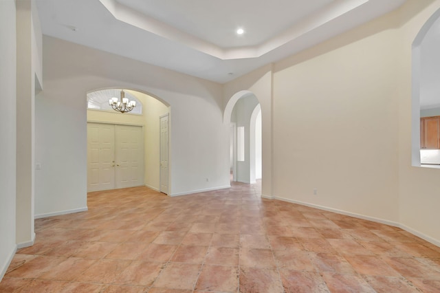 empty room featuring a raised ceiling and an inviting chandelier