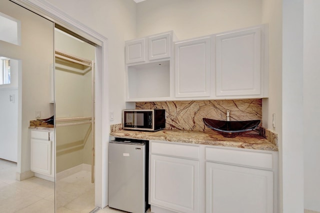 kitchen with white cabinetry, tasteful backsplash, light tile patterned floors, and stainless steel refrigerator