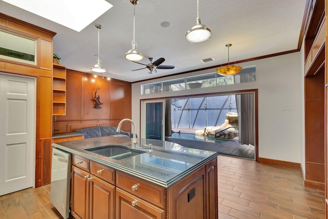 kitchen with a kitchen island with sink, ornamental molding, sink, light wood-type flooring, and a skylight