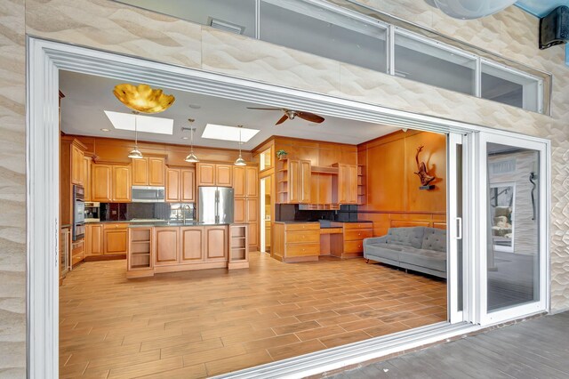 kitchen featuring appliances with stainless steel finishes, a skylight, ceiling fan, decorative light fixtures, and light hardwood / wood-style flooring