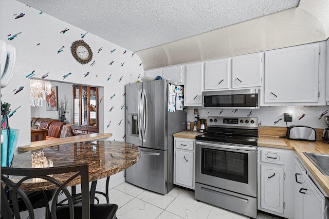 kitchen featuring white cabinetry, stainless steel appliances, a notable chandelier, and a textured ceiling