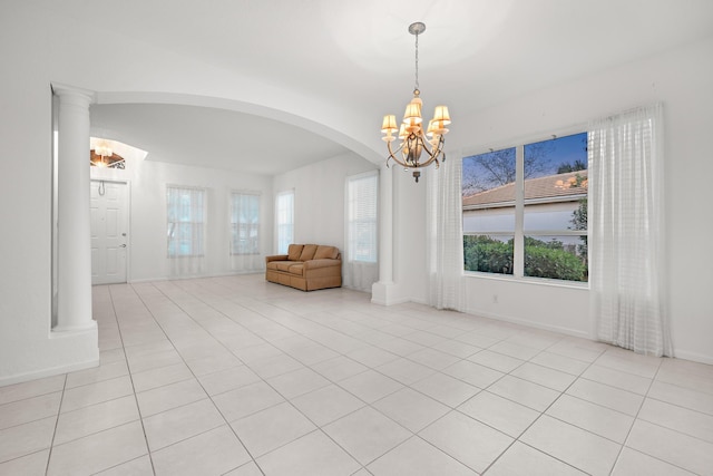 tiled spare room with decorative columns and an inviting chandelier