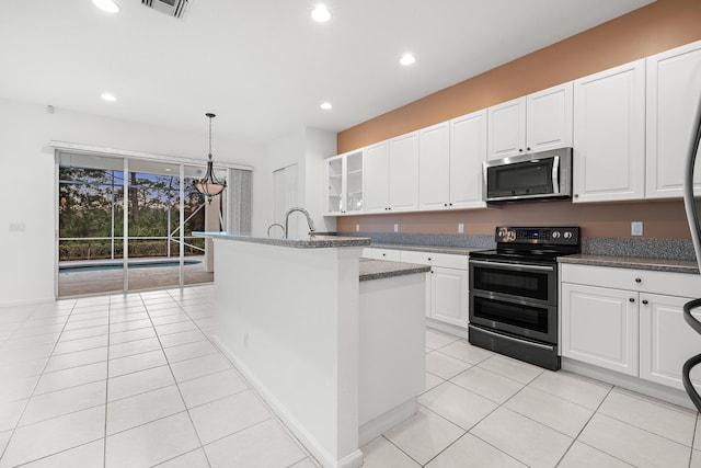 kitchen featuring appliances with stainless steel finishes, light tile patterned flooring, white cabinetry, decorative light fixtures, and a kitchen island with sink