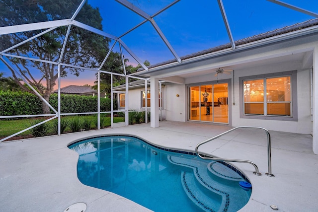 pool at dusk with a patio area, glass enclosure, and ceiling fan