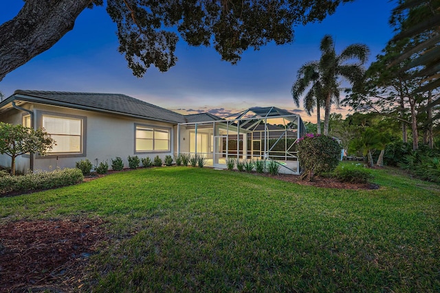 back house at dusk with a lanai and a lawn