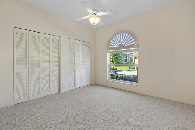 unfurnished bedroom featuring carpet, two closets, and ceiling fan