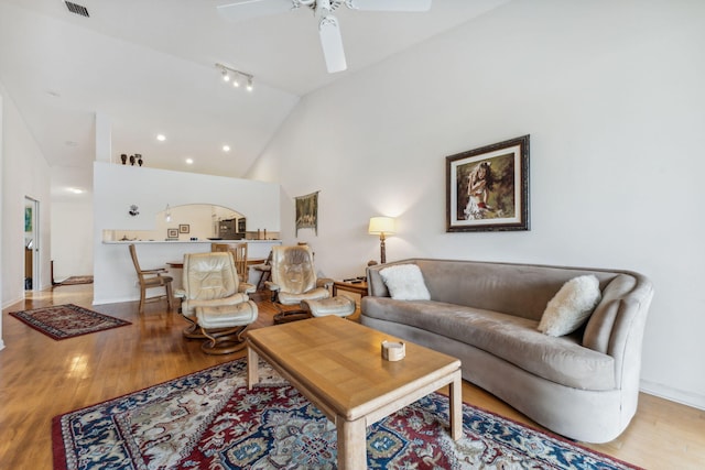 living room with baseboards, visible vents, a ceiling fan, light wood-type flooring, and high vaulted ceiling