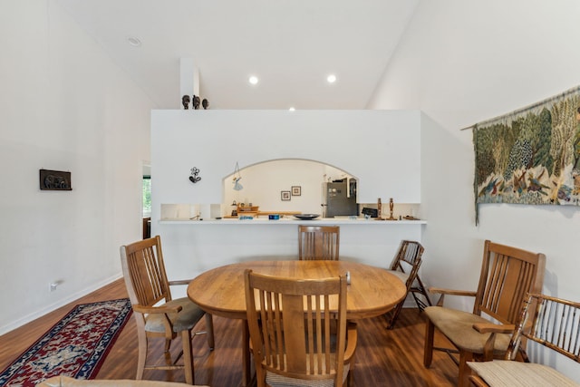 dining area featuring baseboards, arched walkways, wood finished floors, high vaulted ceiling, and recessed lighting