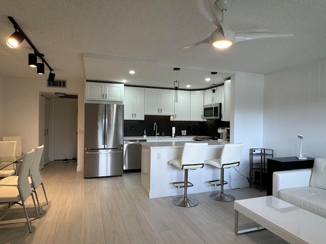 kitchen featuring appliances with stainless steel finishes, white cabinetry, a textured ceiling, and a kitchen breakfast bar