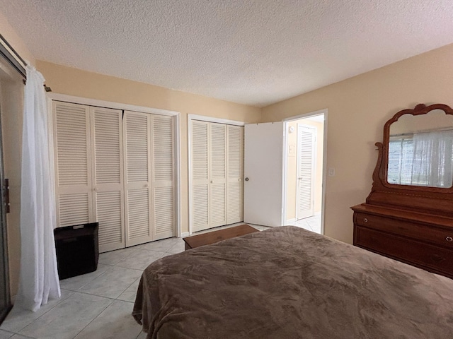 bedroom with multiple closets, light tile patterned flooring, and a textured ceiling