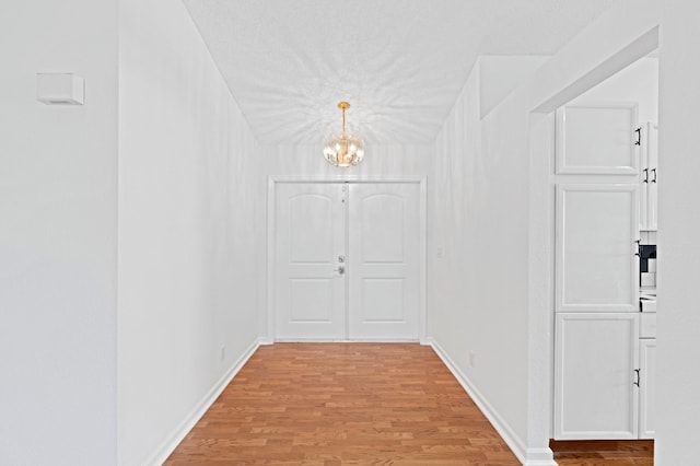 corridor with a textured ceiling, a chandelier, and light wood-type flooring