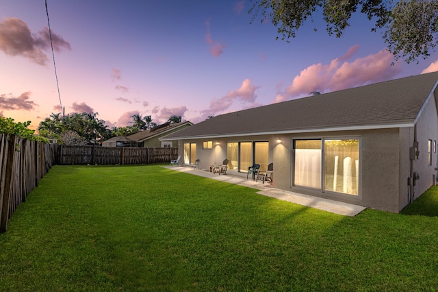 back house at dusk with a patio and a lawn