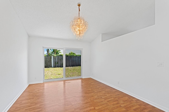 empty room with hardwood / wood-style floors, a textured ceiling, and a chandelier