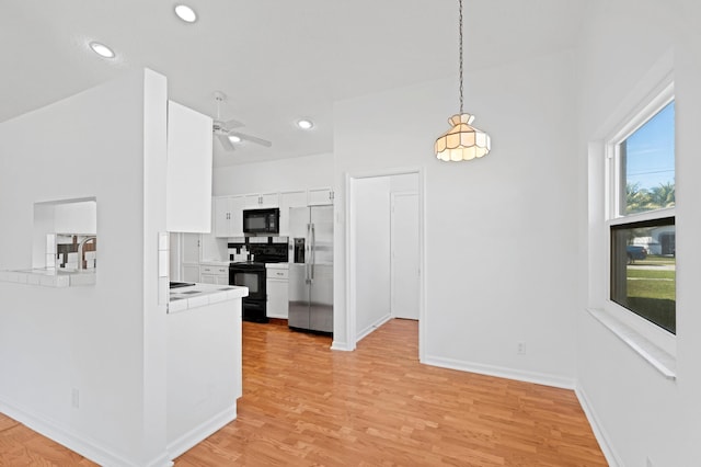 kitchen with white cabinets, hanging light fixtures, tile counters, black appliances, and light wood-type flooring