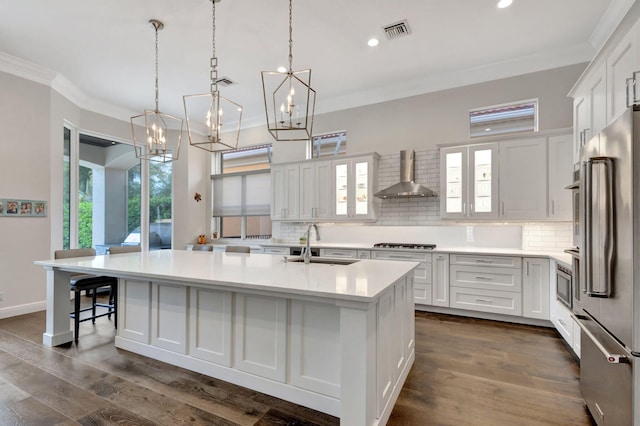 kitchen with a sink, visible vents, high end fridge, ornamental molding, and wall chimney range hood