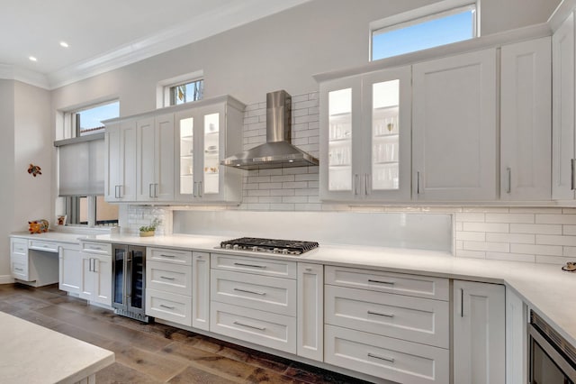 kitchen featuring decorative backsplash, appliances with stainless steel finishes, wall chimney exhaust hood, beverage cooler, and white cabinets