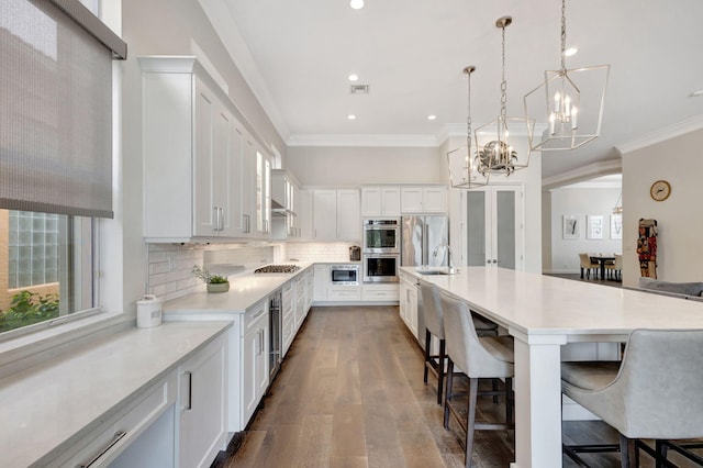 kitchen featuring a kitchen breakfast bar, backsplash, a large island with sink, pendant lighting, and white cabinets