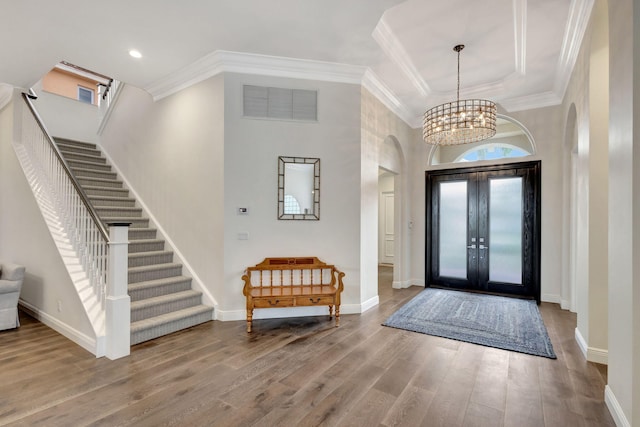 foyer with crown molding, a towering ceiling, a chandelier, and hardwood / wood-style flooring