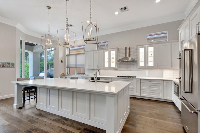 kitchen featuring visible vents, high end refrigerator, a sink, wall chimney exhaust hood, and a notable chandelier