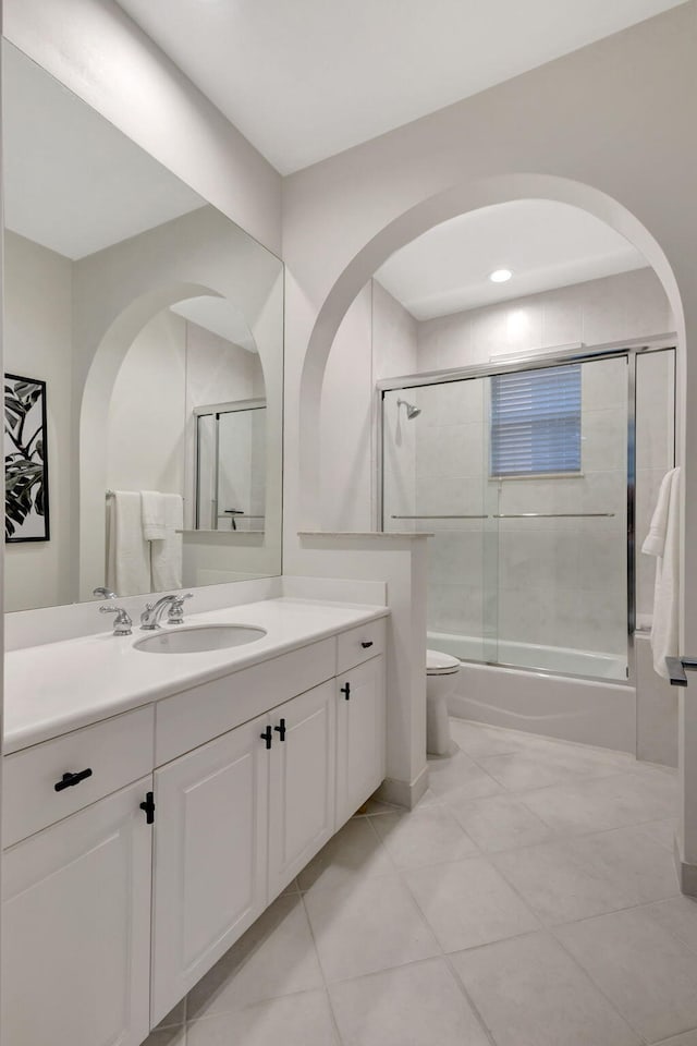 full bathroom with shower / bath combination with glass door, tile patterned flooring, vanity, and toilet