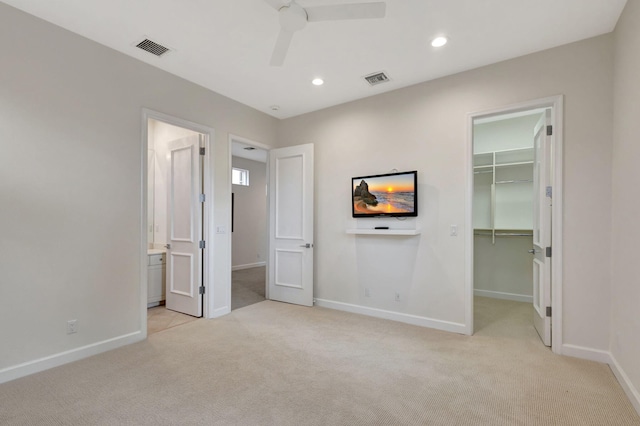 unfurnished bedroom featuring light carpet, ensuite bathroom, ceiling fan, a spacious closet, and a closet