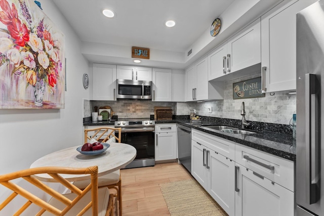 kitchen with stainless steel appliances, light wood-type flooring, white cabinetry, backsplash, and sink