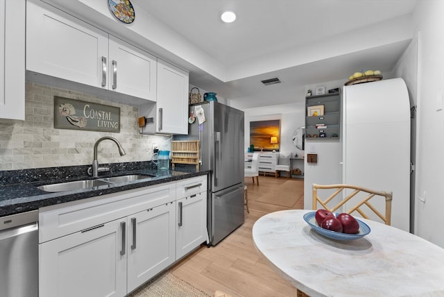 kitchen with stainless steel appliances, light hardwood / wood-style floors, sink, dark stone countertops, and white cabinets