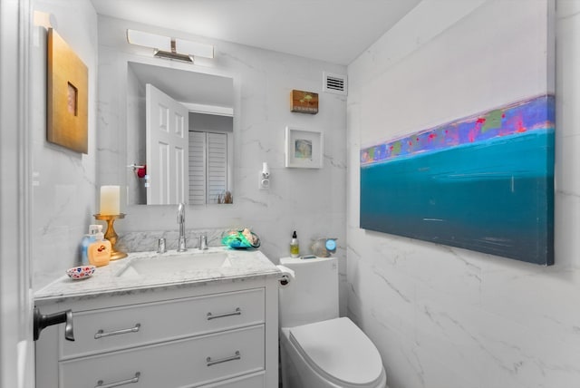 bathroom with toilet, vanity, and tile walls