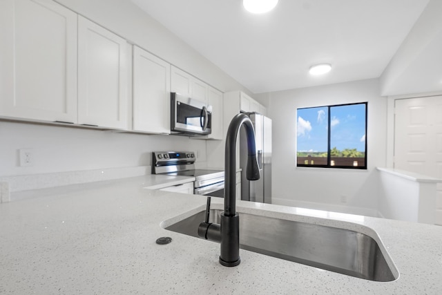 kitchen with white cabinetry, sink, light stone counters, and appliances with stainless steel finishes