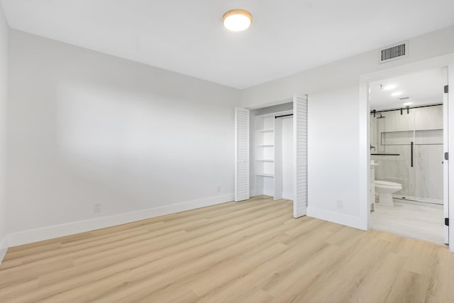 unfurnished bedroom featuring ensuite bathroom, a closet, and light wood-type flooring