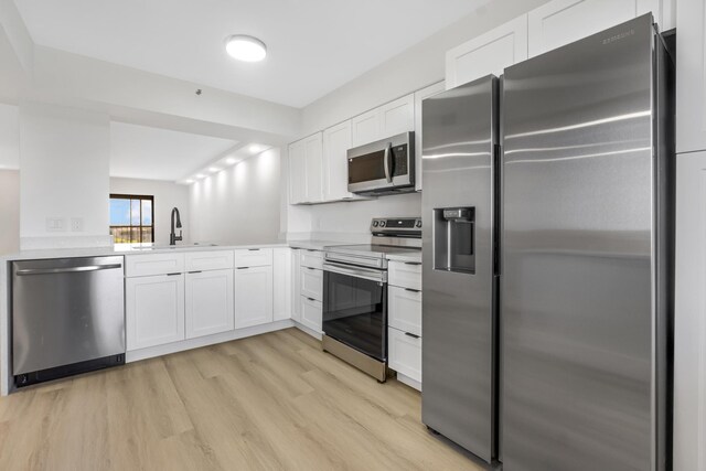 kitchen with stainless steel appliances, white cabinets, sink, and light wood-type flooring