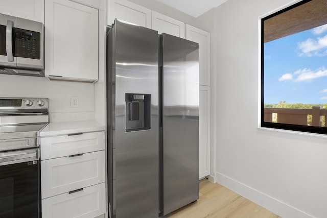 kitchen with white cabinets, light stone countertops, appliances with stainless steel finishes, and light hardwood / wood-style flooring