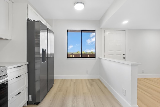 kitchen featuring white cabinets, stainless steel fridge, light wood-type flooring, and kitchen peninsula