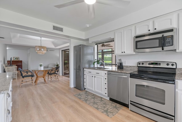 kitchen featuring hanging light fixtures, white cabinetry, a tray ceiling, light hardwood / wood-style flooring, and stainless steel appliances