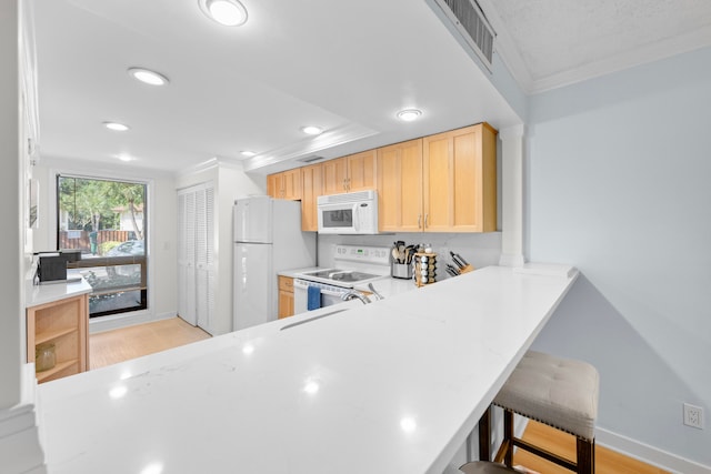 kitchen with a breakfast bar area, kitchen peninsula, ornamental molding, light wood-type flooring, and white appliances