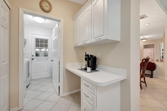 interior space featuring washing machine and clothes dryer, light tile patterned flooring, a textured ceiling, built in desk, and white cabinets