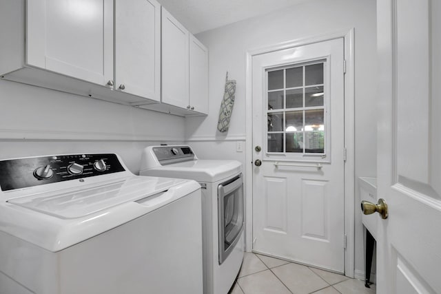 clothes washing area with washer and dryer, cabinets, and light tile patterned flooring