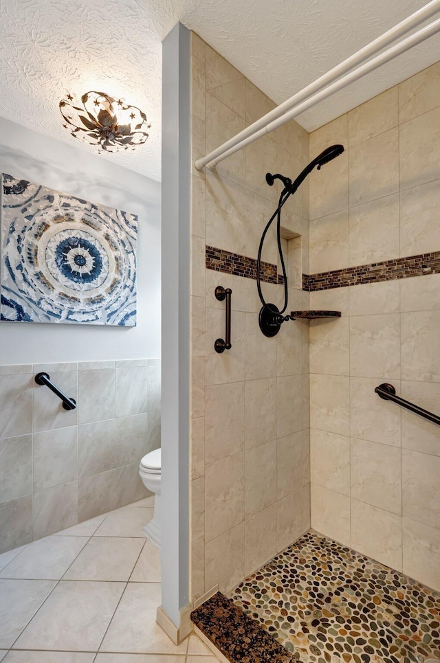 bathroom with tile patterned floors, tiled shower, tile walls, and toilet