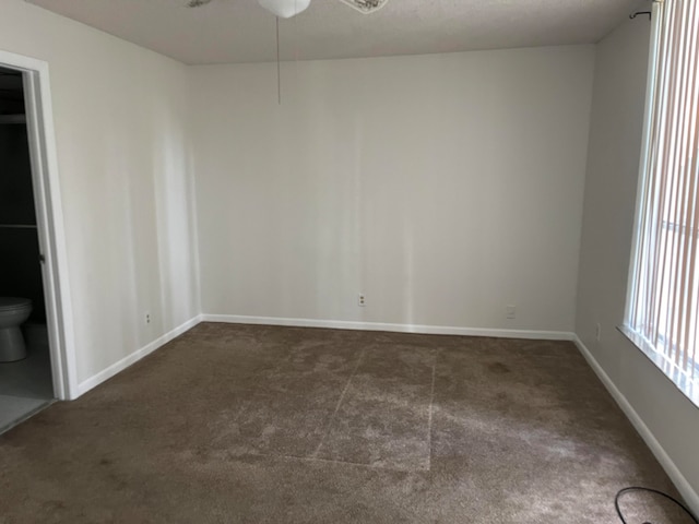 spare room featuring ceiling fan and dark carpet