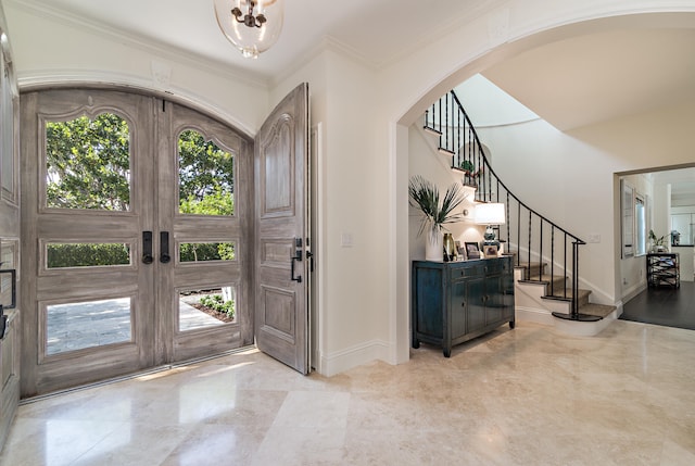 foyer with french doors, a chandelier, and crown molding