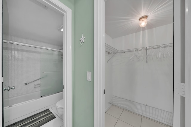 bathroom with tile patterned floors, combined bath / shower with glass door, and toilet