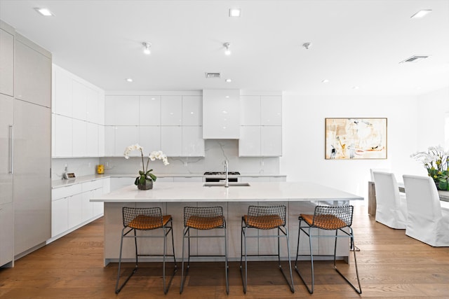 kitchen with a kitchen breakfast bar, white cabinetry, light wood-type flooring, and a kitchen island with sink