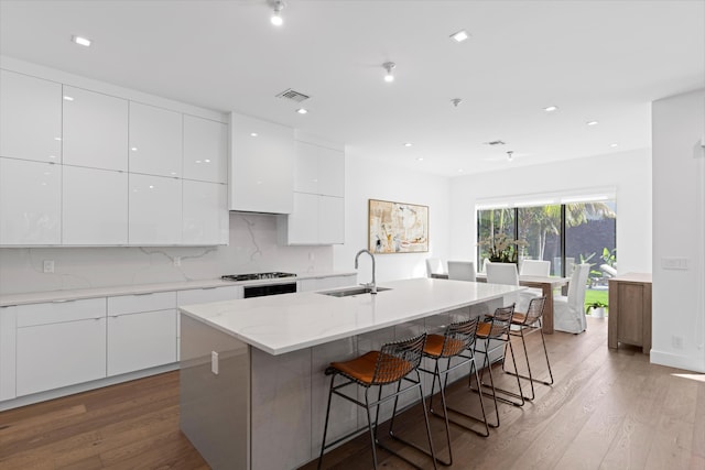 kitchen with white cabinets, sink, wood-type flooring, and an island with sink