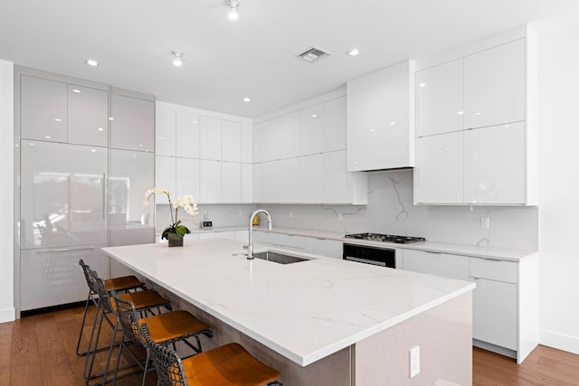 kitchen with a kitchen bar, a center island with sink, and white cabinets